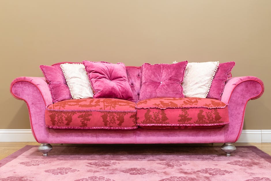 A white upholstered sofa with tufted detailing along the backrest and rolled arms, positioned against a white wall with decorative paneling in a well-lit room. The sofa's fabric appears clean and fres